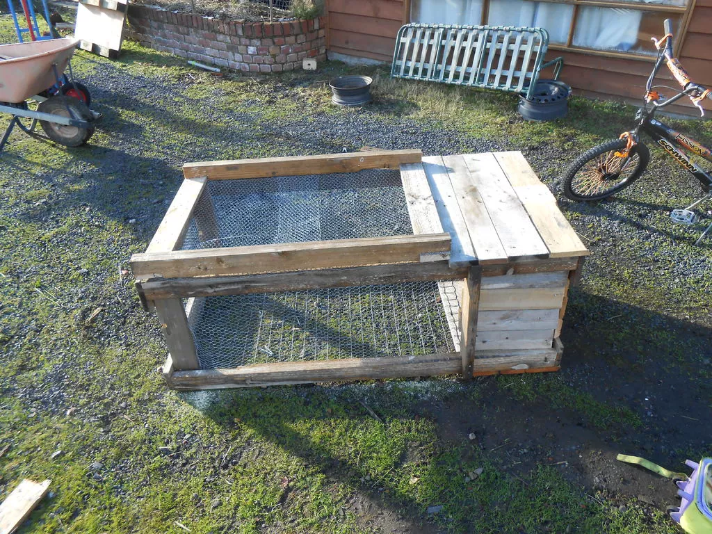 A small rabbit hutch in a yard near a bicycle.